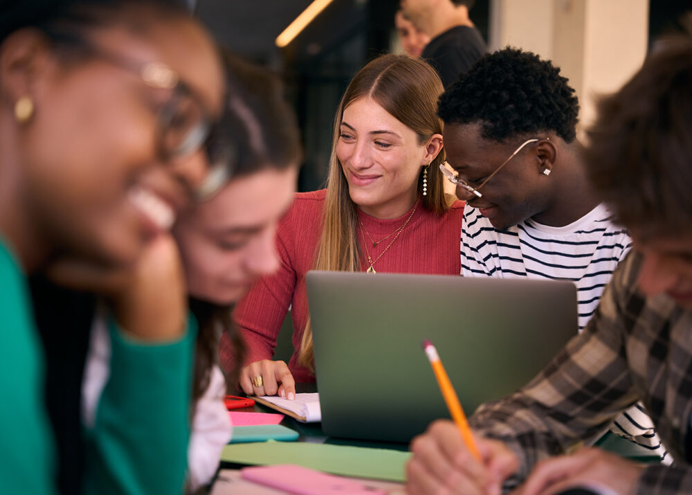 Selective focus on smiling young girl and a black guy studying together with workbooks using laptop